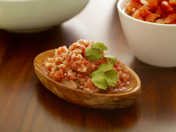 Small wood bowl of pico de gallo on a wood table garnished with parsley