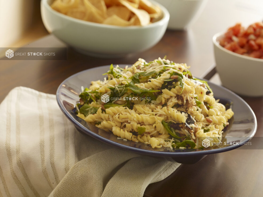 Bowl of pasta salad with spinach and pine nuts on a wood table