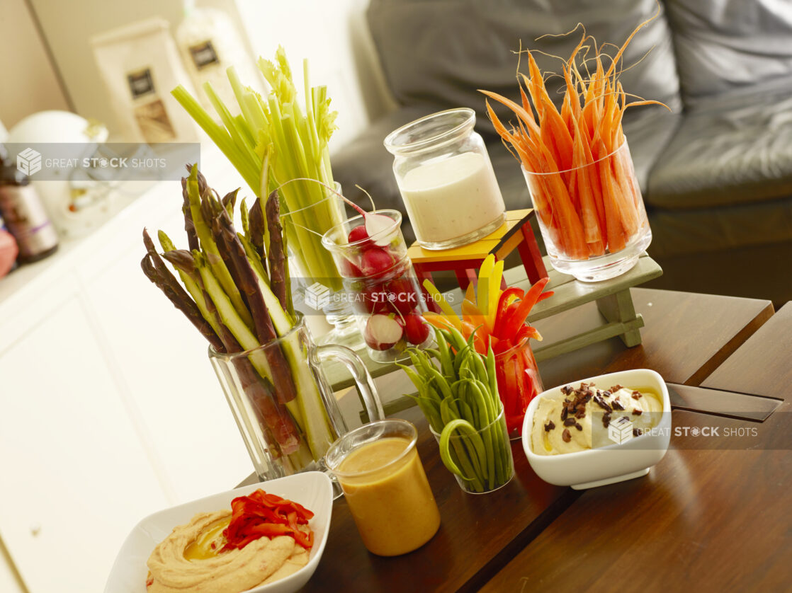 Assortment of hummus and dips with vegetable sticks on a wood table in a house