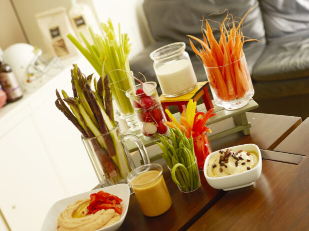 Assortment of hummus and dips with vegetable sticks on a wood table in a house