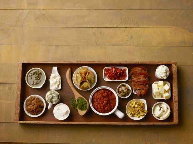 Large wood tray of toppings for a meal on a wood table