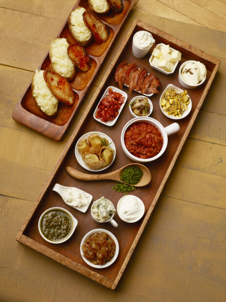 Large wood tray of toppings for a baked potatoes on a wood table