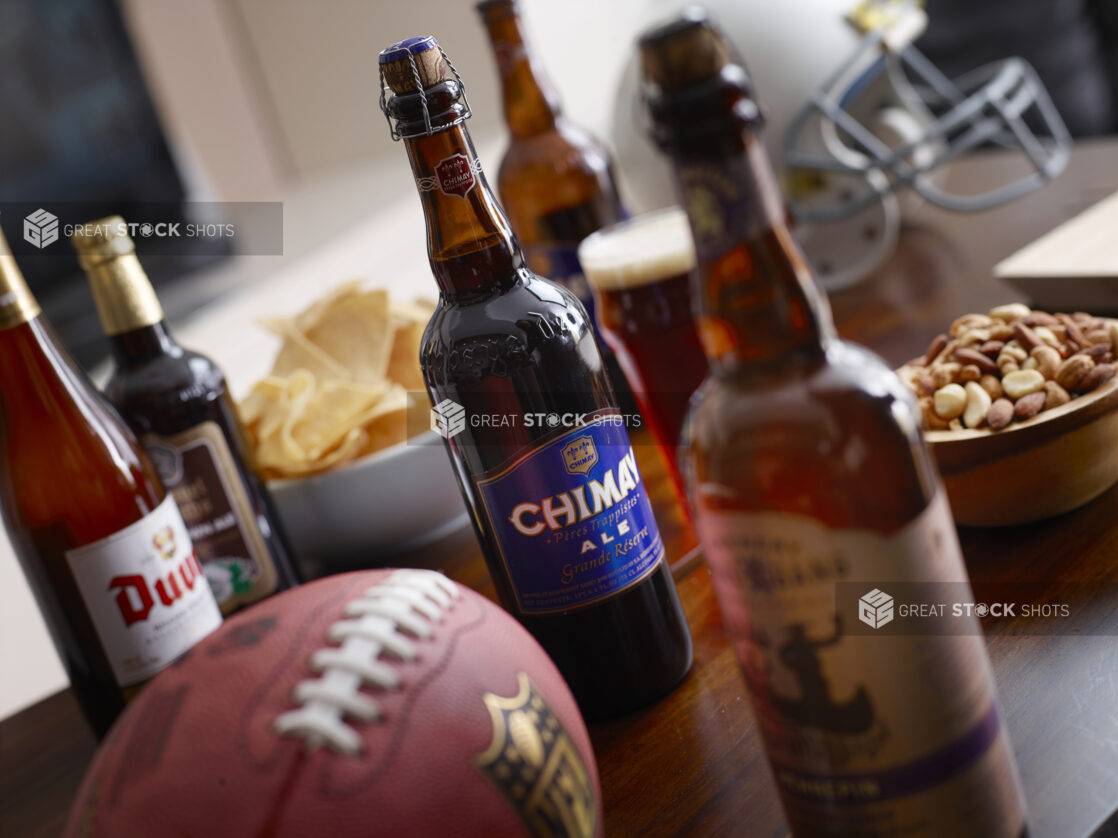 Bottles of Belgian beer on a living room wooden table with snacks, a helmet and football