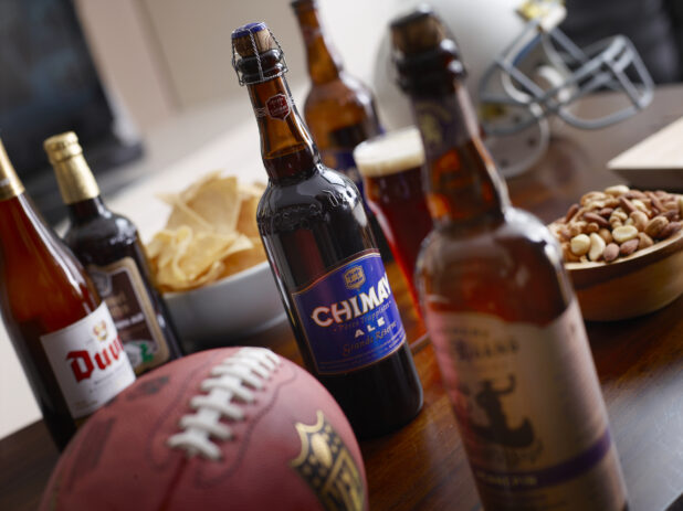 Bottles of Belgian beer on a living room wooden table with snacks, a helmet and football