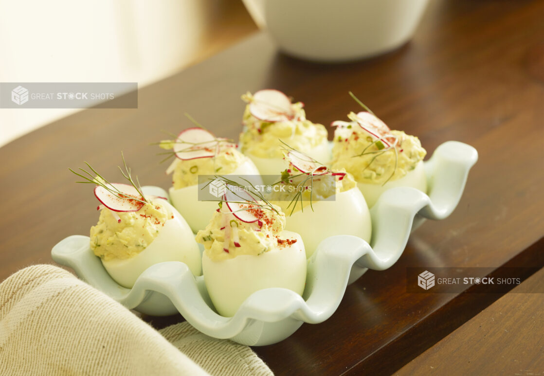 Half dozen standing deviled eggs topped with fresh dill, chives and radish slice on a wood table