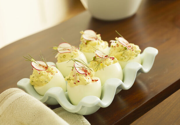 Half dozen standing deviled eggs topped with fresh dill, chives and radish slice on a wood table