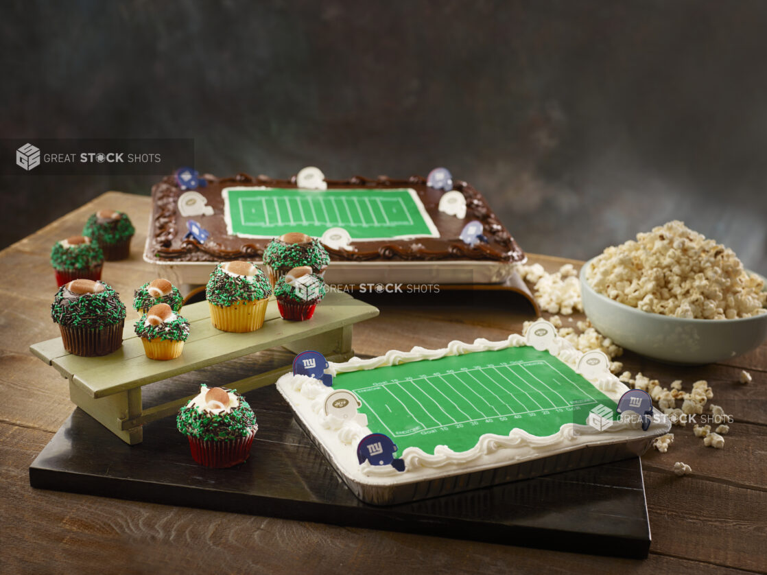 Two football themed cakes with football field and sprinkle cupcakes with edible footballs and a bowl of popcorn for a themed party