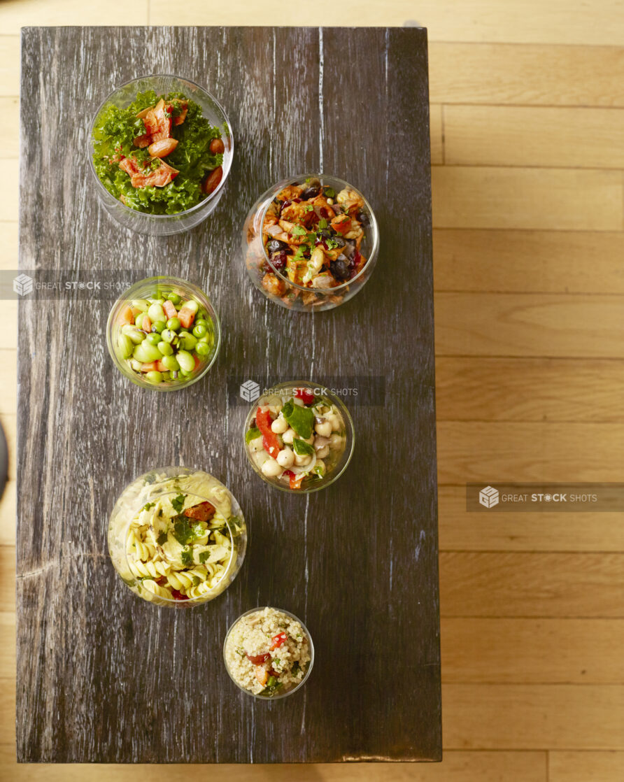 Overhead of various glass of vegetarian salads on a wood table