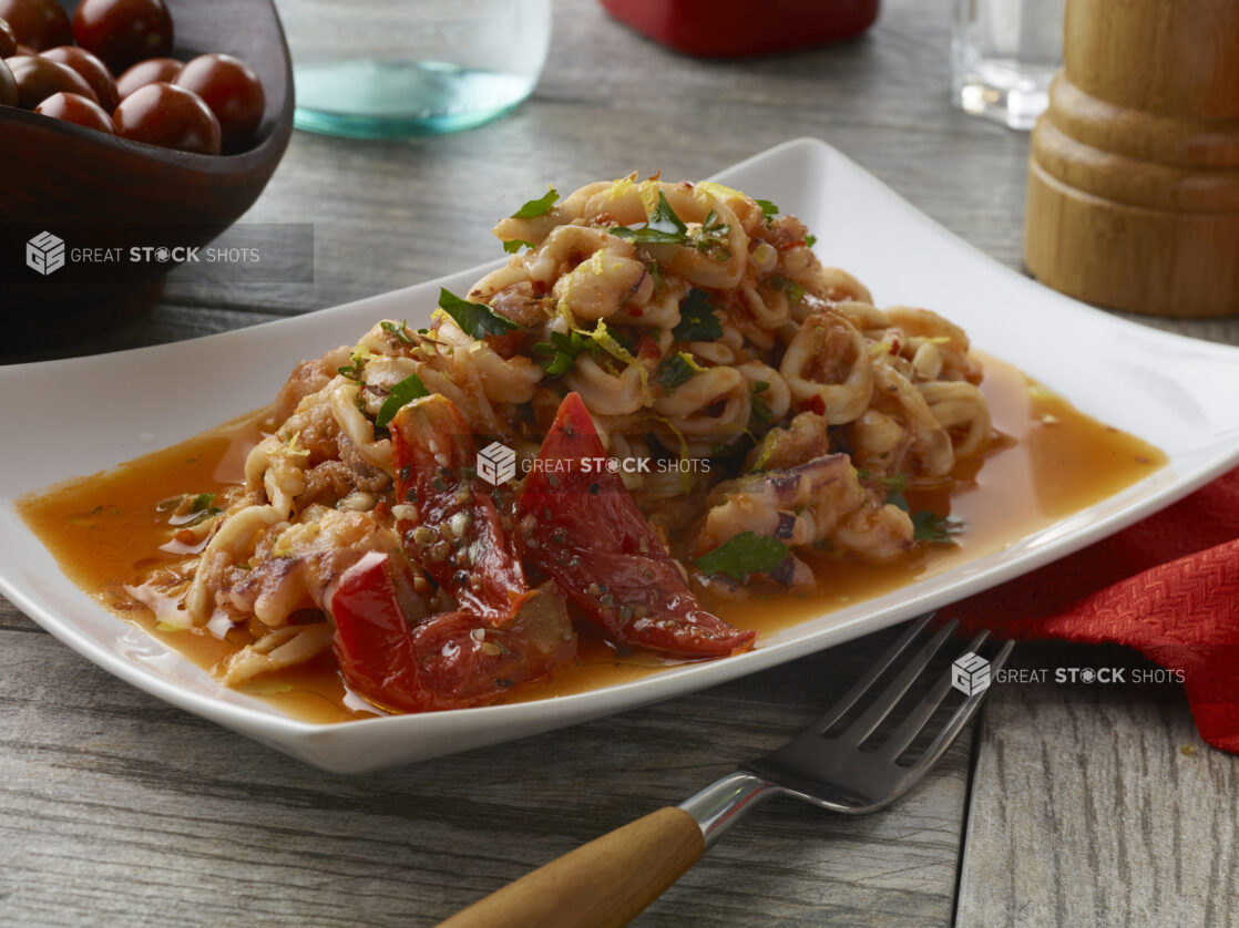 Sautéed calamari in a thin tomato sauce with sun-dried tomatoes topped with fresh parsley and lemon zest on a wood table