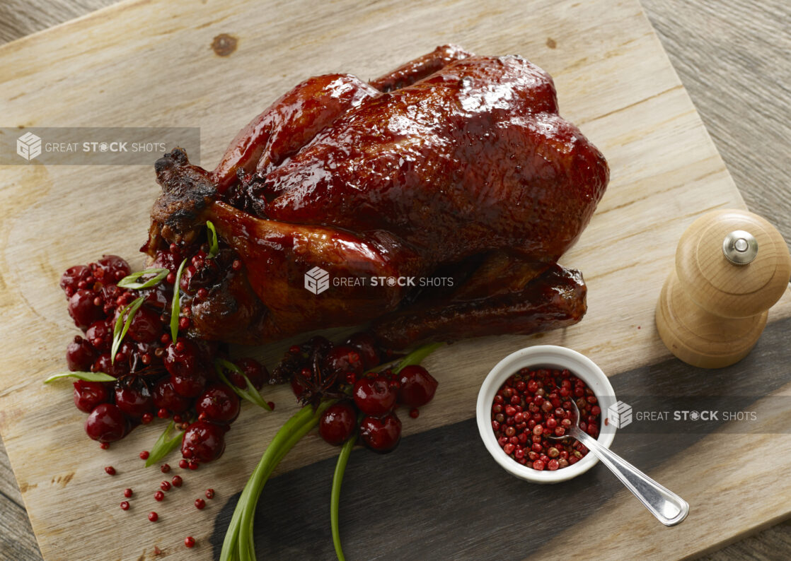 Whole cranberry glazed turkey stuffed with whole cranberries, pink peppercorn and green onion on a wooden board