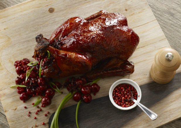 Whole cranberry glazed turkey stuffed with whole cranberries, pink peppercorn and green onion on a wooden board
