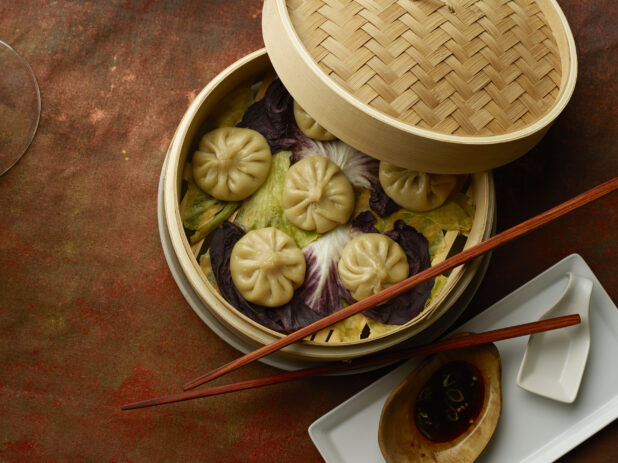 Overhead of steamed soup dumplings in a bamboo basket with chop sticks and lid on the side