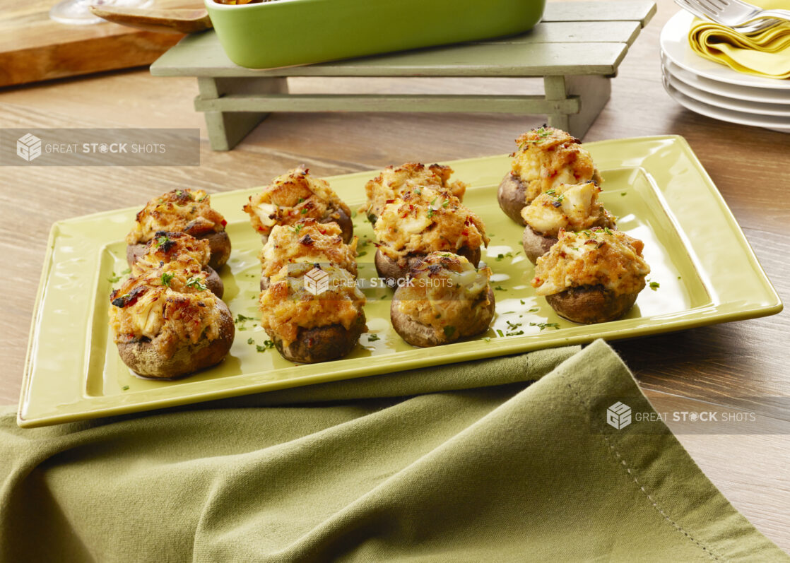 Dozen seafood and cheese stuffed mushroom caps on a green platter with a green napkin on a wood table