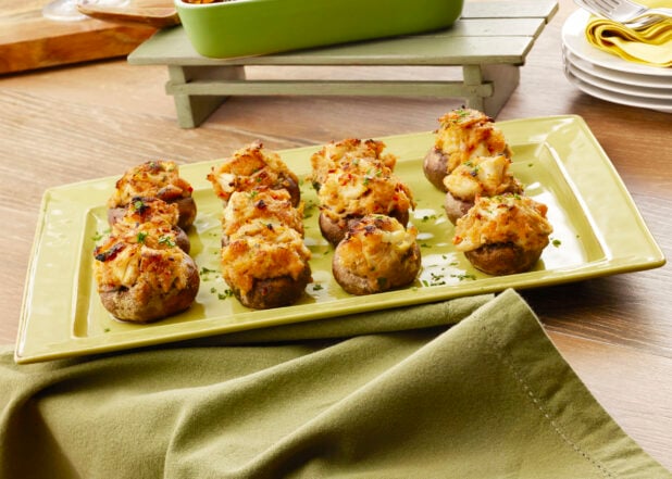 Dozen seafood and cheese stuffed mushroom caps on a green platter with a green napkin on a wood table