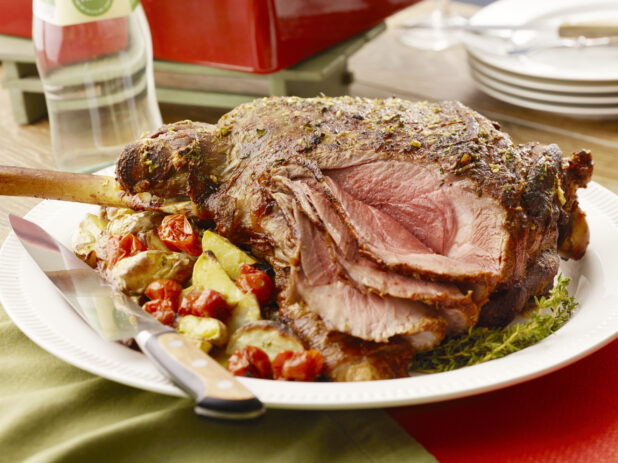 Large sliced bone in prime rib roast on a white serving platter with roasted potatoes and cherry tomatoes