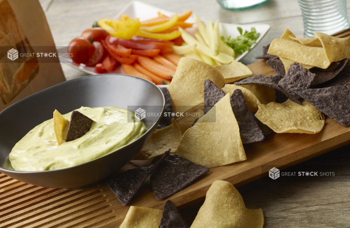 Green goddess dip with tortilla chips and fresh cut vegetables on a wood table