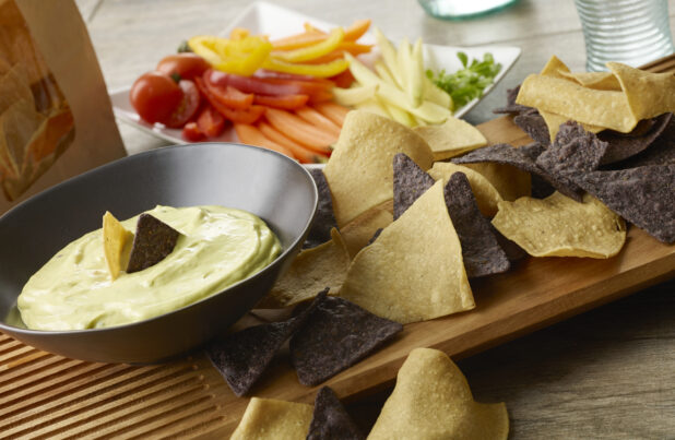 Green goddess dip with tortilla chips and fresh cut vegetables on a wood table