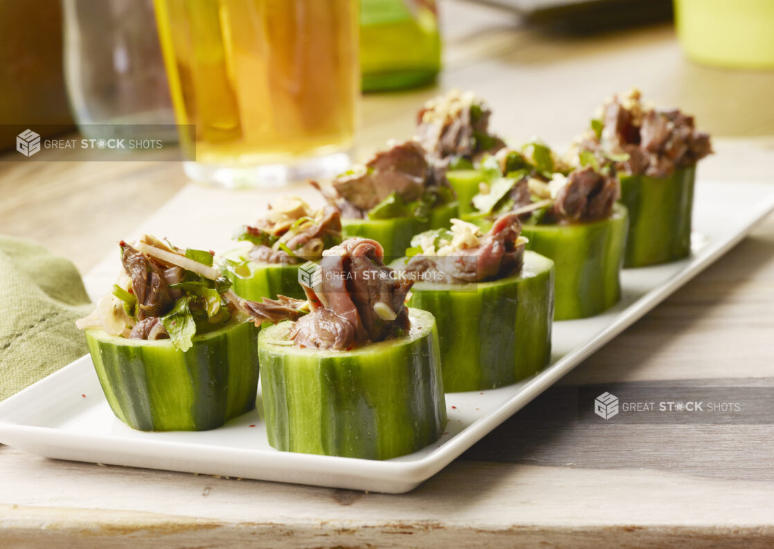 White tray of Thai roast beef cucumber cups appetizers on a wood table