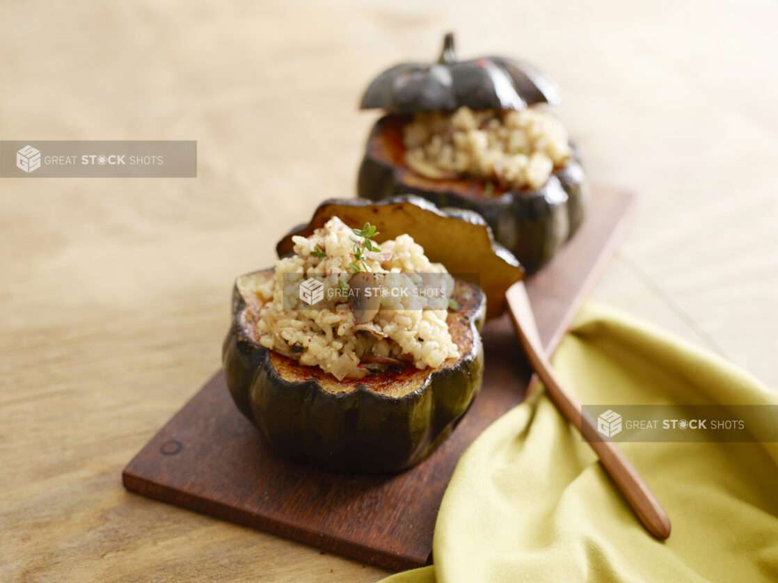 Two acorn squash stuffed with rice and sautéed mushrooms and onion on a wood board on a wood table