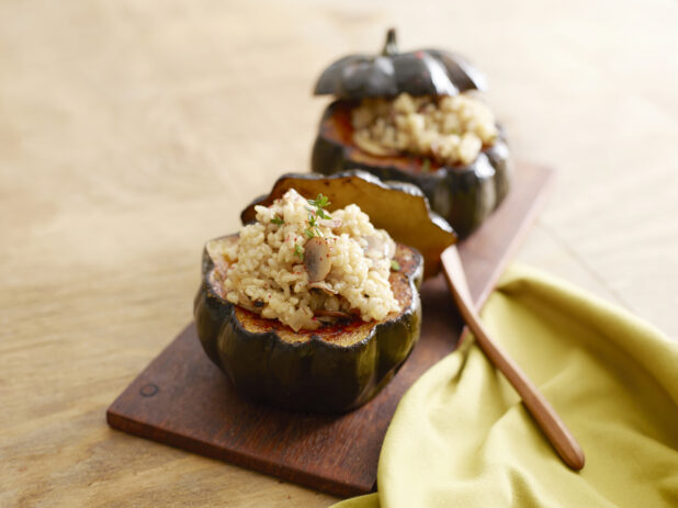 Two acorn squash stuffed with rice and sautéed mushrooms and onion on a wood board on a wood table