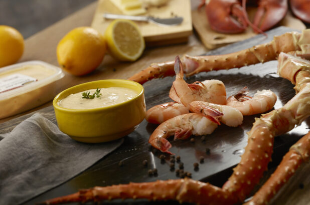 Shrimp, crab legs and lobster claws on a wooden board with a creamy dipping sauce with fresh lemon in the background