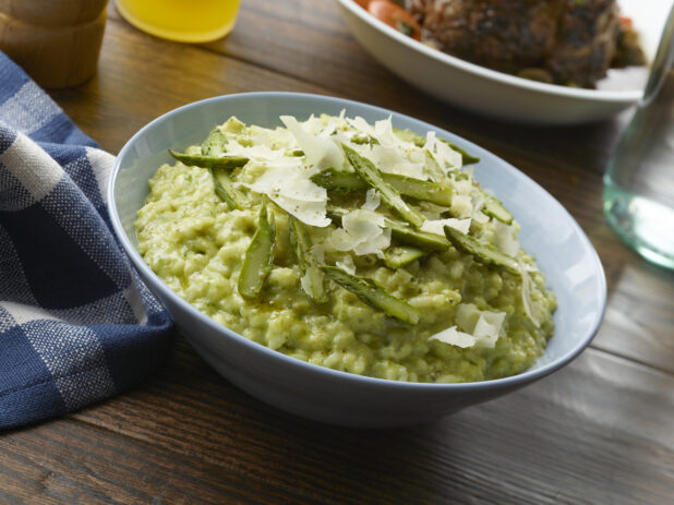 Bowl of green risotto topped with sliced asparagus pepper and fresh shaved parmesan cheese on a wood table