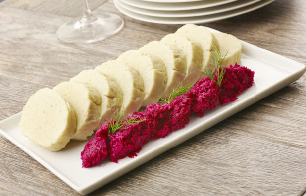 Sliced gefilte fish with chrein on a white wooden plate on a wooden table