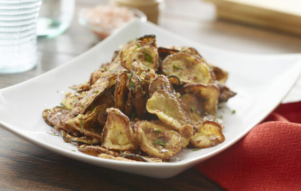 White bowl of fried vegetable chips on a wood table