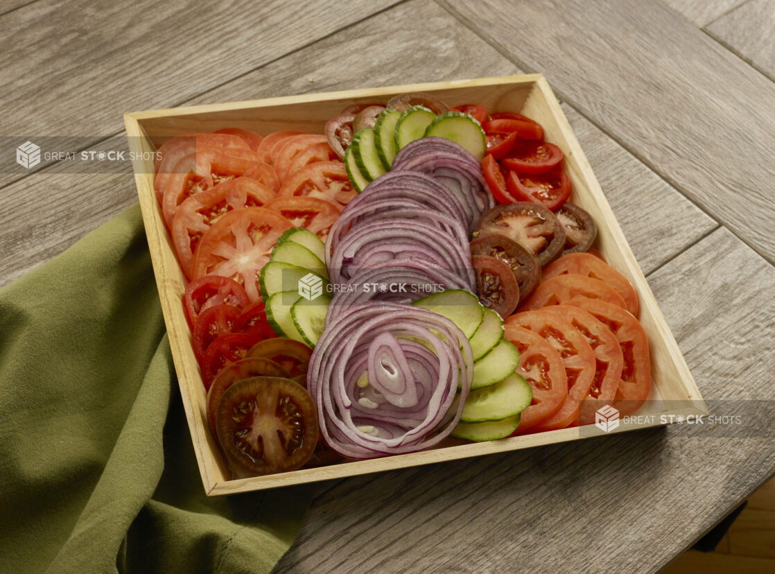 Wood catering tay with a variety of sliced tomatoes, red onion and cucumbers on a wood table with a napkin