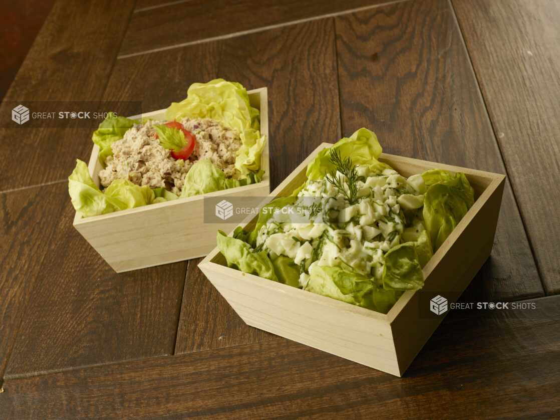 Wood catering bowls of tuna and egg white salad lined with lettuce leafs on a wood table