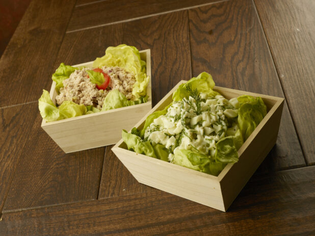 Wood catering bowls of tuna and egg white salad lined with lettuce leafs on a wood table