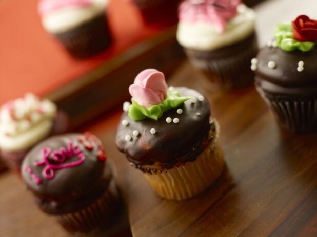Valentine's Day cupcakes decorated with roses, handwriting and candy pearls with chocolate and vanilla frosting on a wood table