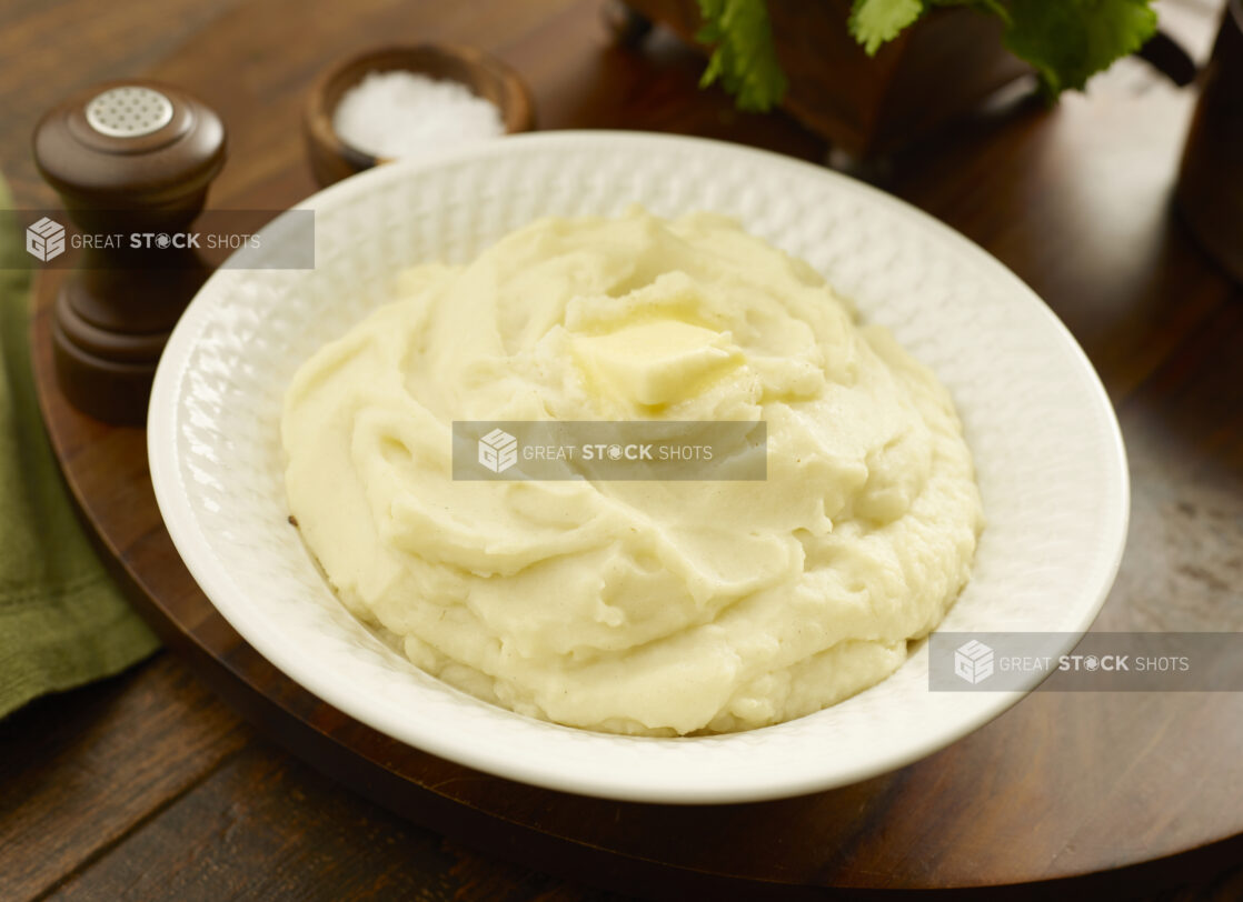 Large bowl of mashed potatoes with a pat of melting butter on top on a wooden board