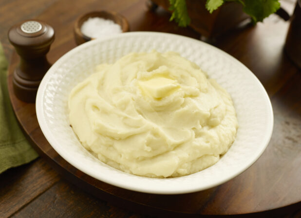 Large bowl of mashed potatoes with a pat of melting butter on top on a wooden board