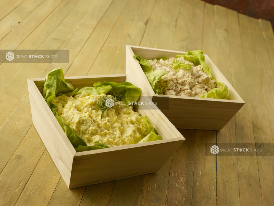 Two wood catering trays with egg and tuna salad on a wood table