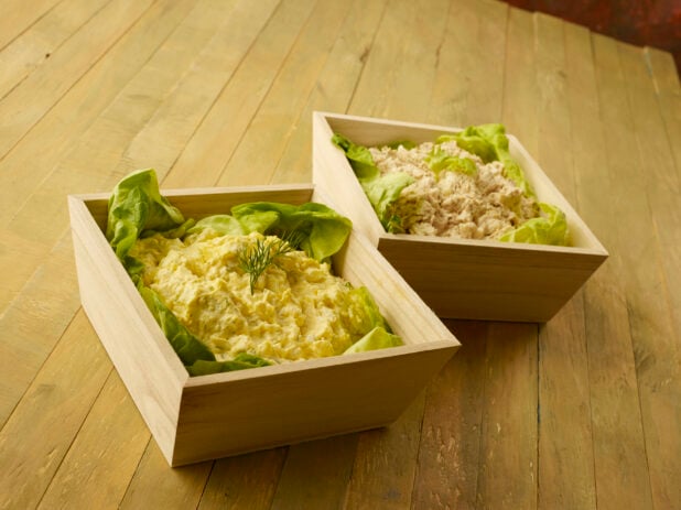 Two wood catering trays with egg and tuna salad on a wood table
