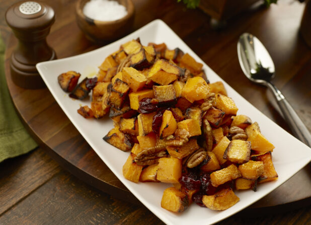 Plate of roasted butternut squash, pecans and cranberries on a wooden board