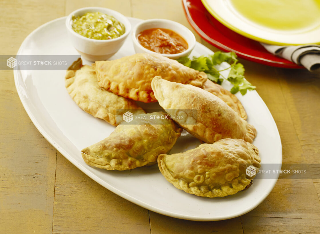 Plate of two flavors of empanadas with two dips on the side on a wood table