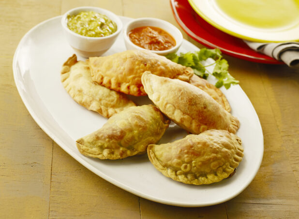 Plate of two flavors of empanadas with two dips on the side on a wood table