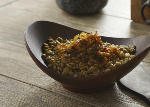 Wooden bowl of lentils with caramelized onion on top on a wood table