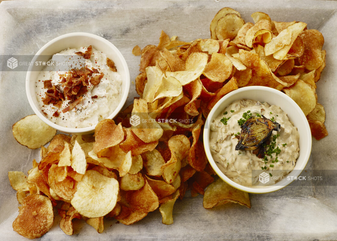 Overhead of kettle cooked chips with an onion, chive dip and a creamy bacon dip on a marble platter