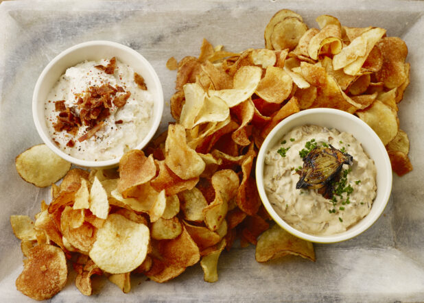 Overhead of kettle cooked chips with an onion, chive dip and a creamy bacon dip on a marble platter