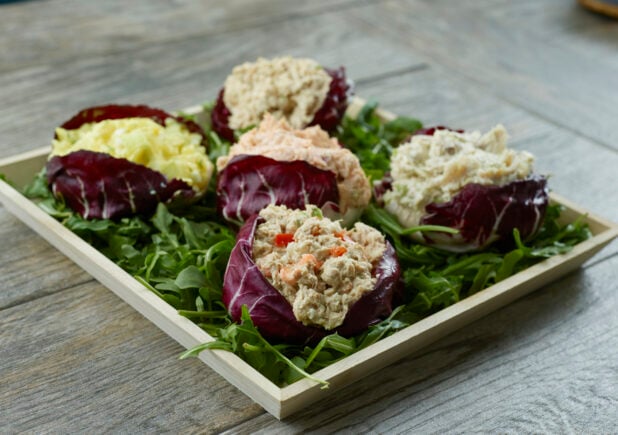 Various spreadable salads for a sandwich in radicchio cups on a bed of arugula in a wood catering tray on a table