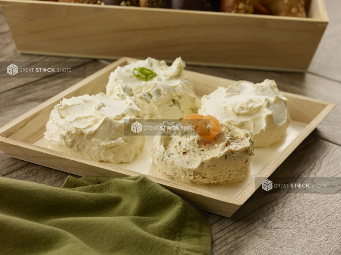 Three flavors of cream cheese in four balls on a wooden catering tray with parchment paper on a wood table