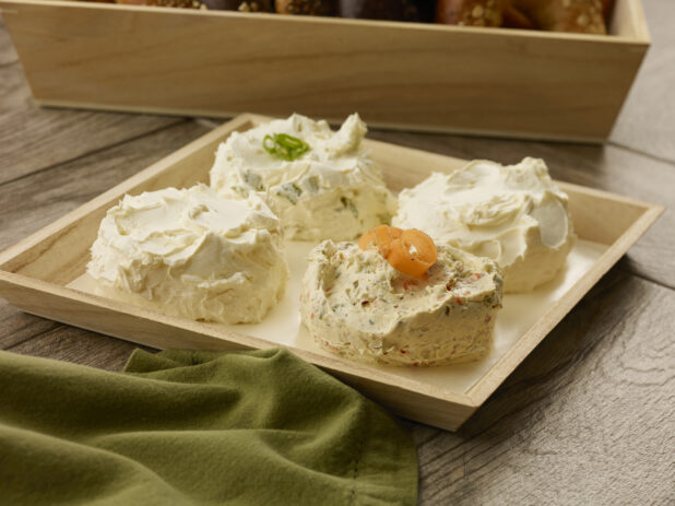 Three flavors of cream cheese in four balls on a wooden catering tray with parchment paper on a wood table