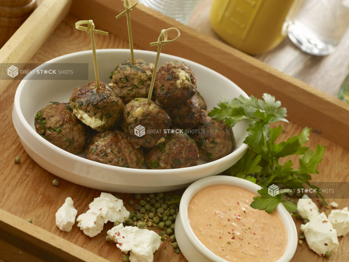 White bowl of goat cheese stuffed meatballs with a creamy orange dipping sauce in a wooden tray with ingredients