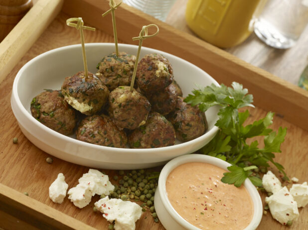 White bowl of goat cheese stuffed meatballs with a creamy orange dipping sauce in a wooden tray with ingredients