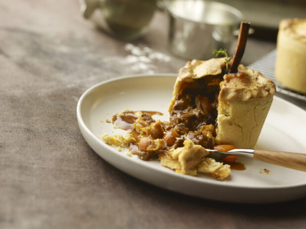 Standing beef pie with bone in the middle, cut down the side with beef and carrots in gravy falling out of the side with a fork