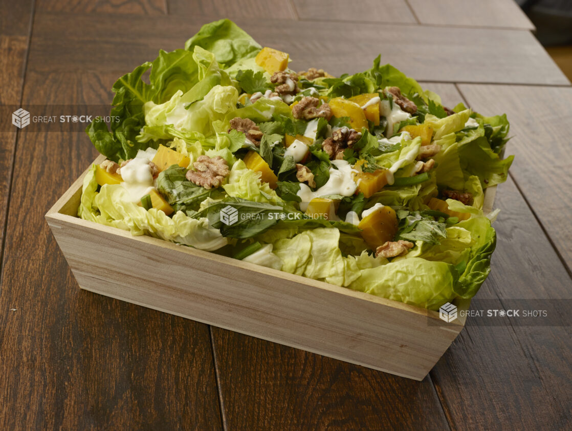 Large salad with romaine, golden beets, walnuts and green beans in a wooden catering bowl drizzled with creamy dressing on a wooden table