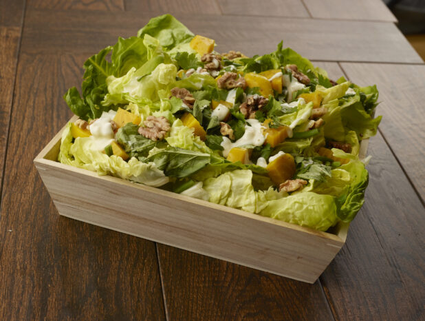 Large salad with romaine, golden beets, walnuts and green beans in a wooden catering bowl drizzled with creamy dressing on a wooden table
